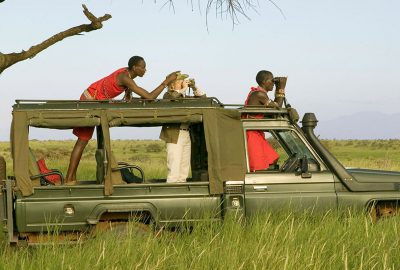 three people on top of a vehicle in a field